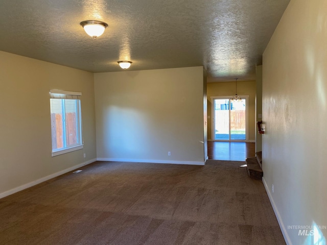 carpeted empty room with a textured ceiling and an inviting chandelier