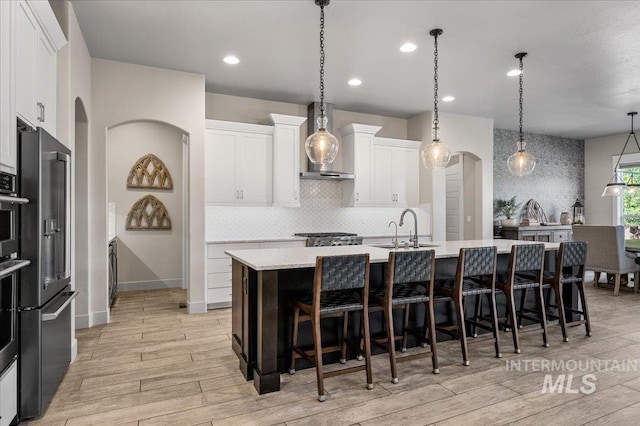 2357 N Synergy Pl, Eagle, ID 83616 - kitchen with arched walkways, wall chimney exhaust hood, light wood finished floors, light countertops, and a center island with sink