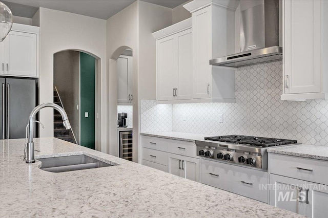 2357 N Synergy Pl, Eagle, ID 83616 - kitchen with wall chimney exhaust hood, appliances with stainless steel finishes, arched walkways, white cabinetry, and beverage cooler