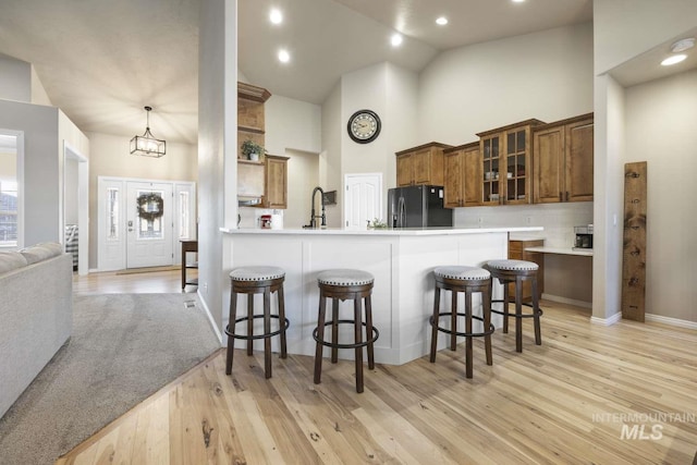 kitchen with light hardwood / wood-style floors, high vaulted ceiling, a breakfast bar, kitchen peninsula, and black refrigerator with ice dispenser