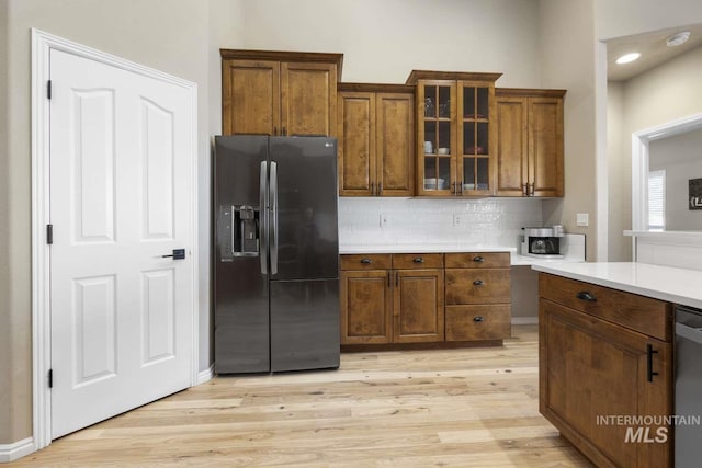 kitchen with dishwasher, light hardwood / wood-style floors, backsplash, and black fridge with ice dispenser