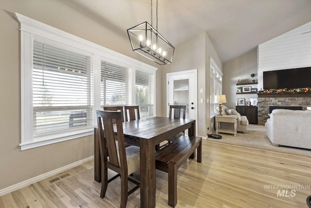 dining space featuring light wood-type flooring, lofted ceiling, a fireplace, and an inviting chandelier