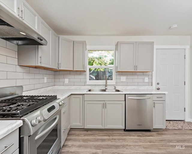 504 E 7th St, Emmett, ID 83617 - kitchen with appliances with stainless steel finishes, a sink, under cabinet range hood, light wood-style flooring, and decorative backsplash