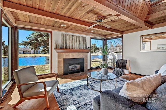 living room featuring a tiled fireplace, wooden ceiling, and a water view