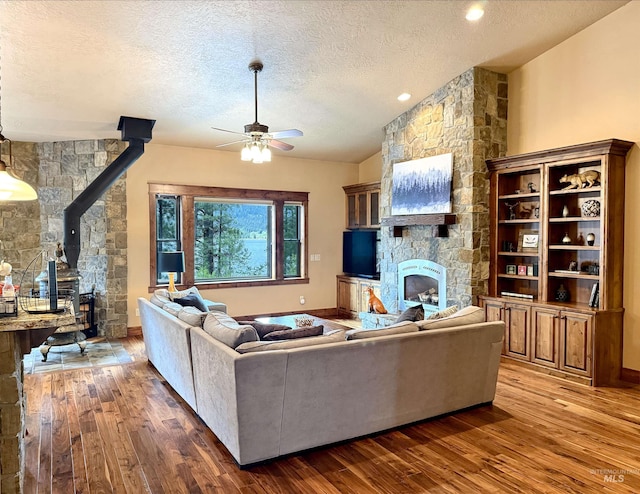 20 Shore Crest Ct, Donnelly, ID 83615 - living room with a wood stove, a ceiling fan, wood-type flooring, a textured ceiling, and a stone fireplace