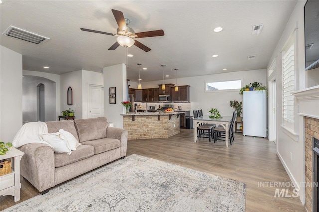 living room with ceiling fan, arched walkways, light wood finished floors, and recessed lighting