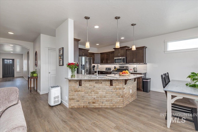 kitchen featuring appliances with stainless steel finishes, dark brown cabinetry, arched walkways, light stone countertops, and a breakfast bar