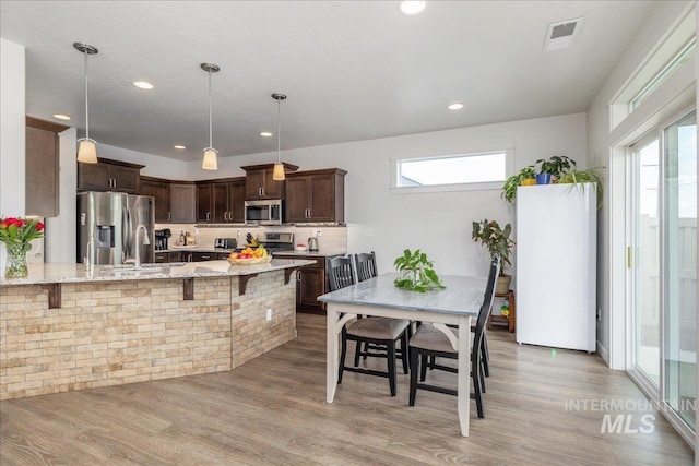 kitchen featuring appliances with stainless steel finishes, dark brown cabinetry, light stone countertops, a kitchen breakfast bar, and recessed lighting