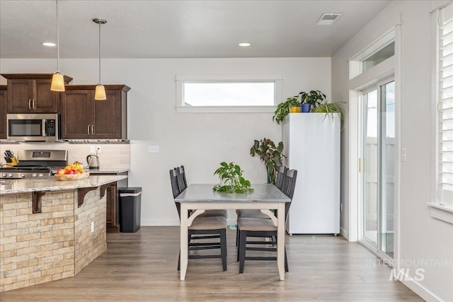 kitchen with appliances with stainless steel finishes, dark brown cabinets, wood finished floors, light stone counters, and recessed lighting