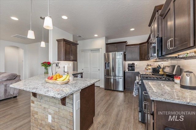 kitchen with appliances with stainless steel finishes, dark brown cabinets, arched walkways, wood finished floors, and recessed lighting