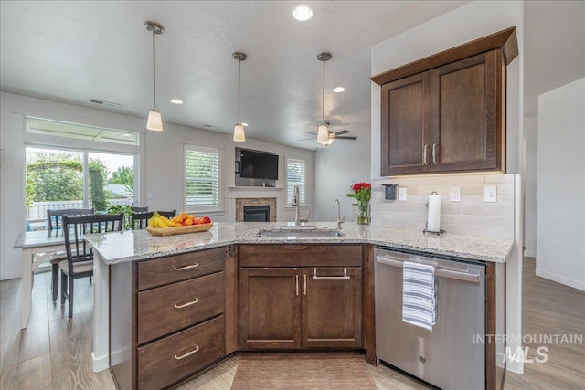kitchen featuring stainless steel dishwasher, a sink, light stone counters, a ceiling fan, and backsplash