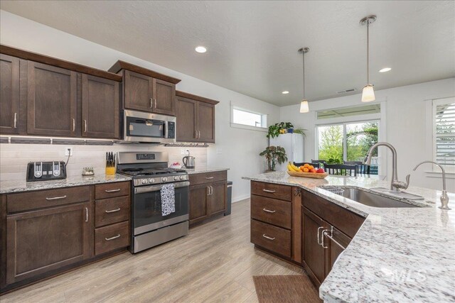 kitchen featuring stainless steel appliances, a sink, tasteful backsplash, light wood-type flooring, and recessed lighting