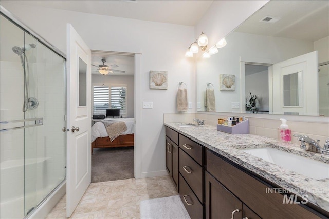 ensuite bathroom featuring a stall shower, double vanity, a ceiling fan, and baseboards
