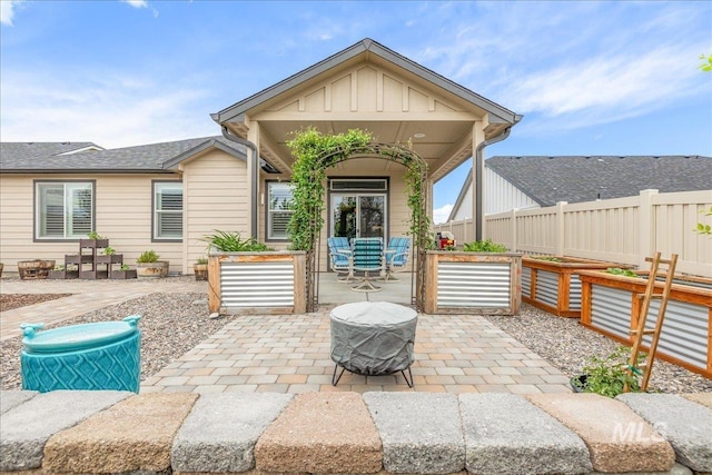 rear view of house with board and batten siding, a patio, a vegetable garden, and fence