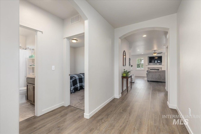 hall with wood finished floors, arched walkways, baseboards, and recessed lighting