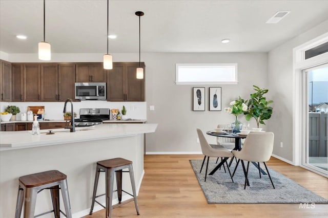 kitchen with stainless steel appliances, light countertops, baseboards, a breakfast bar, and decorative light fixtures