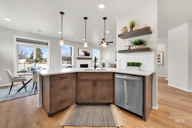 kitchen featuring open shelves, stainless steel dishwasher, a sink, light wood-style floors, and a fireplace