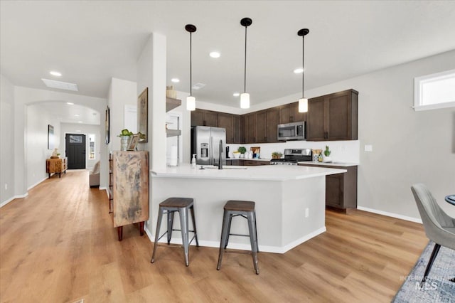 kitchen with light countertops, dark brown cabinets, arched walkways, light wood-style flooring, and appliances with stainless steel finishes