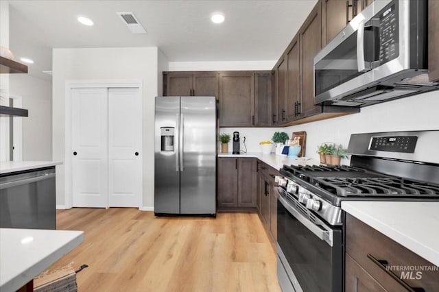kitchen with dark brown cabinetry, appliances with stainless steel finishes, light wood-style floors, and light countertops