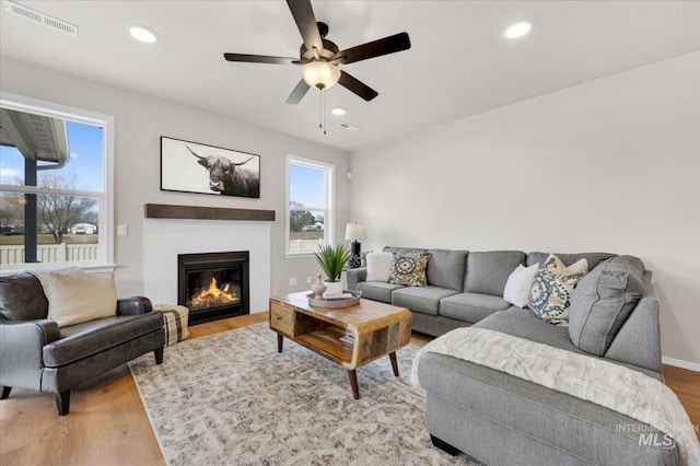 living room featuring recessed lighting, visible vents, light wood-type flooring, a glass covered fireplace, and ceiling fan