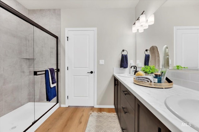 full bathroom featuring a tile shower, wood finished floors, double vanity, and a sink
