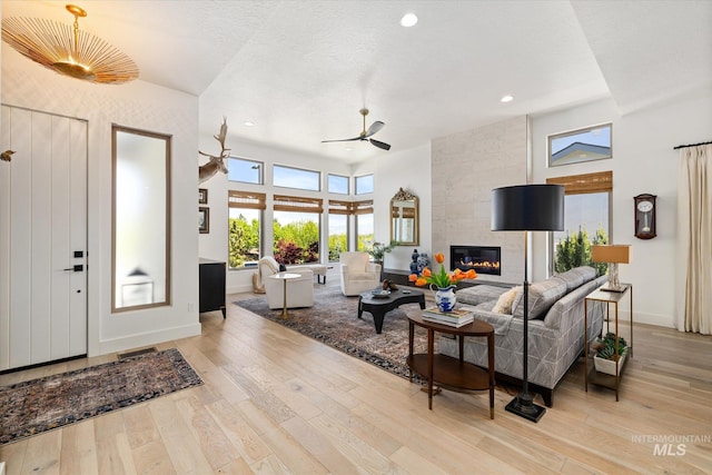 living room with baseboards, a ceiling fan, a large fireplace, and light wood-style flooring