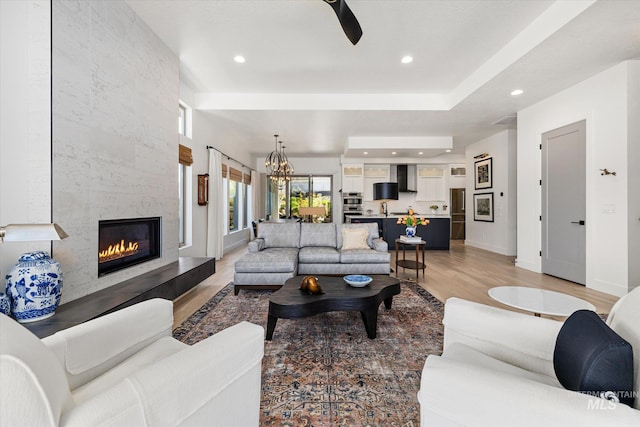 living area featuring recessed lighting, a high end fireplace, light wood-style flooring, and ceiling fan with notable chandelier