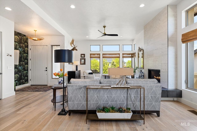 living room with a tiled fireplace, ceiling fan, recessed lighting, and light wood-style flooring