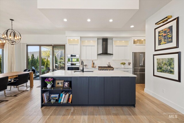 kitchen featuring appliances with stainless steel finishes, a sink, wall chimney exhaust hood, white cabinetry, and modern cabinets