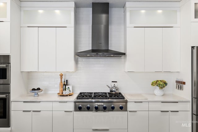 kitchen featuring wall chimney range hood, white cabinets, stainless steel gas stovetop, and backsplash