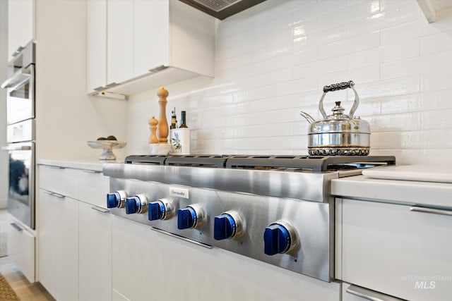 interior space with white cabinets, stainless steel appliances, backsplash, and light countertops