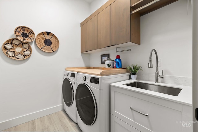 laundry area featuring cabinet space, a sink, baseboards, light wood-style flooring, and washer and clothes dryer