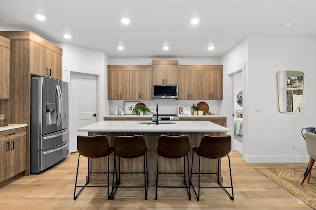 kitchen with tasteful backsplash, an island with sink, a breakfast bar area, stainless steel appliances, and light countertops