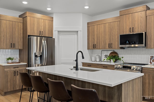 kitchen with light wood-style flooring, appliances with stainless steel finishes, a kitchen breakfast bar, light countertops, and a sink