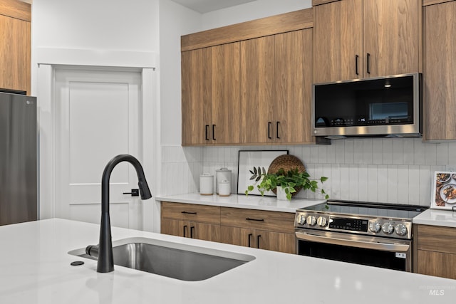 kitchen with appliances with stainless steel finishes, decorative backsplash, a sink, and light countertops