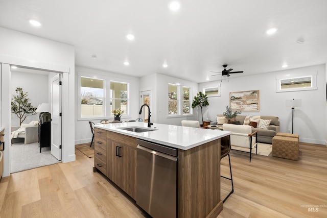 kitchen with a center island with sink, light wood-style flooring, stainless steel dishwasher, a sink, and recessed lighting