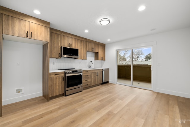 kitchen with stainless steel appliances, light countertops, backsplash, a sink, and light wood-type flooring