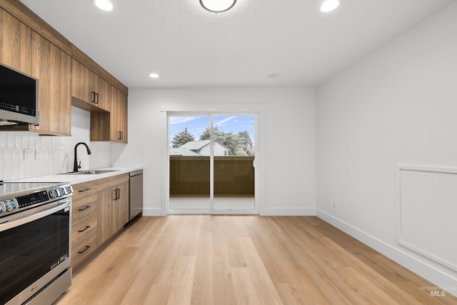 kitchen with stainless steel appliances, light wood-style floors, a sink, and decorative backsplash