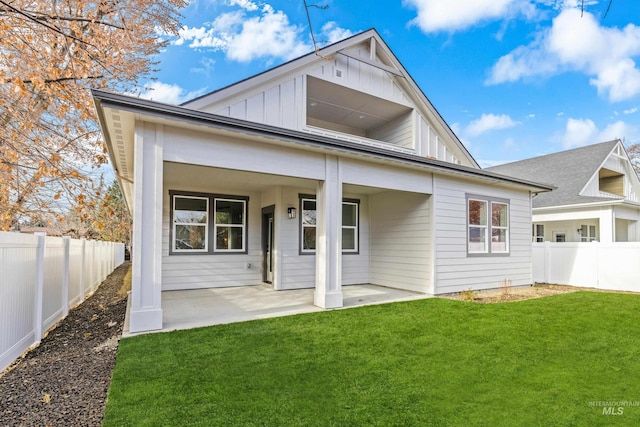 rear view of property featuring board and batten siding, a patio area, a fenced backyard, and a lawn