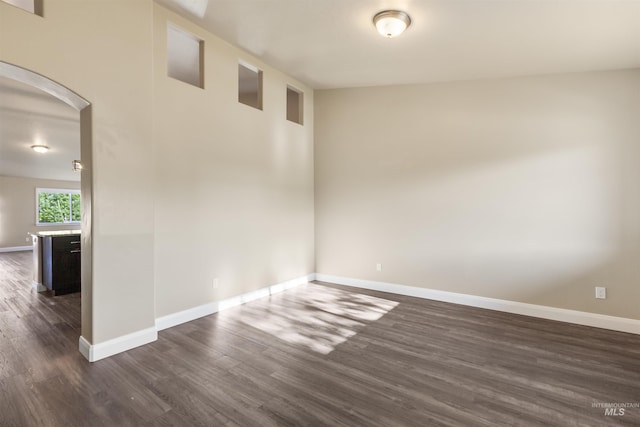 spare room with dark wood-style flooring, arched walkways, and baseboards