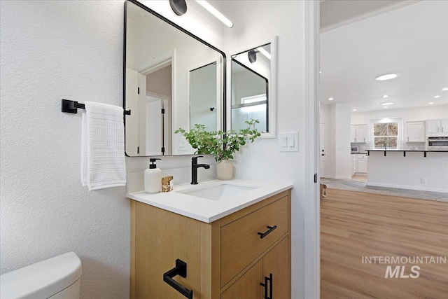 bathroom with toilet, wood finished floors, recessed lighting, vanity, and a textured wall