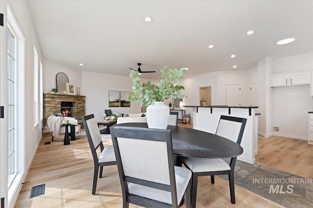 dining area with visible vents, baseboards, recessed lighting, a stone fireplace, and light wood-style floors