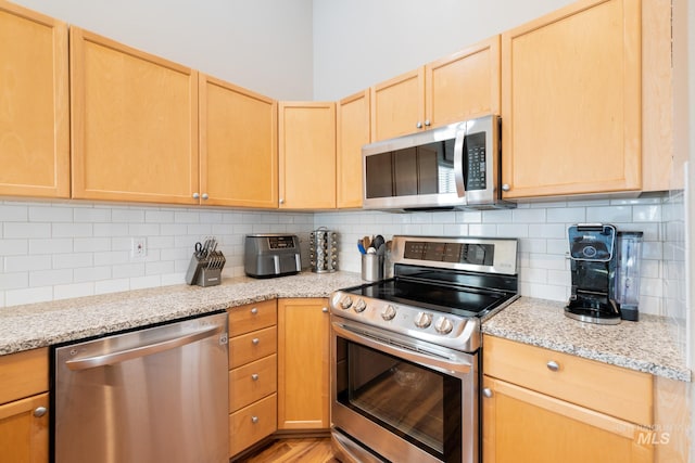 kitchen with light stone counters, appliances with stainless steel finishes, light brown cabinetry, and backsplash