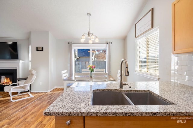 kitchen featuring pendant lighting, sink, backsplash, light stone counters, and light hardwood / wood-style floors