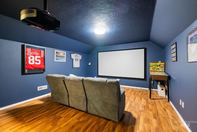 home theater room featuring hardwood / wood-style flooring, vaulted ceiling, and a textured ceiling