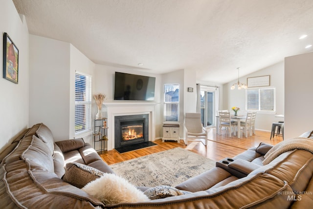 living room featuring lofted ceiling, a notable chandelier, light hardwood / wood-style flooring, and a textured ceiling