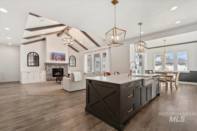 kitchen with wood finished floors, a sink, beam ceiling, a fireplace, and a notable chandelier