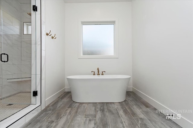 bathroom featuring a stall shower, a soaking tub, wood finished floors, and baseboards