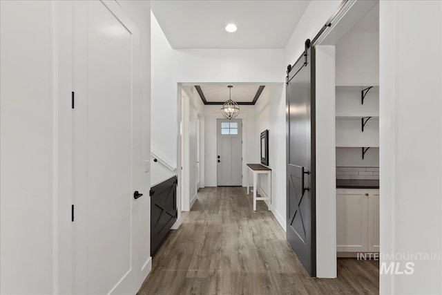 hall featuring a barn door, crown molding, baseboards, and wood finished floors