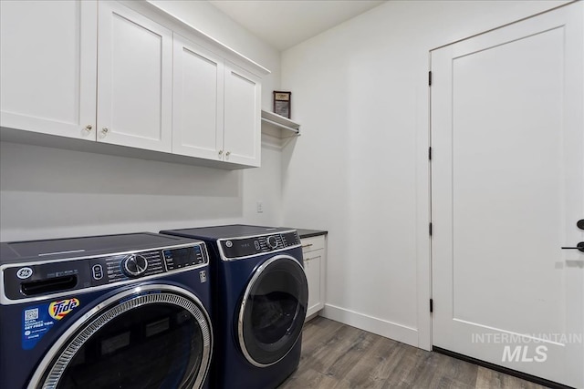 clothes washing area with dark wood finished floors, washing machine and clothes dryer, cabinet space, and baseboards